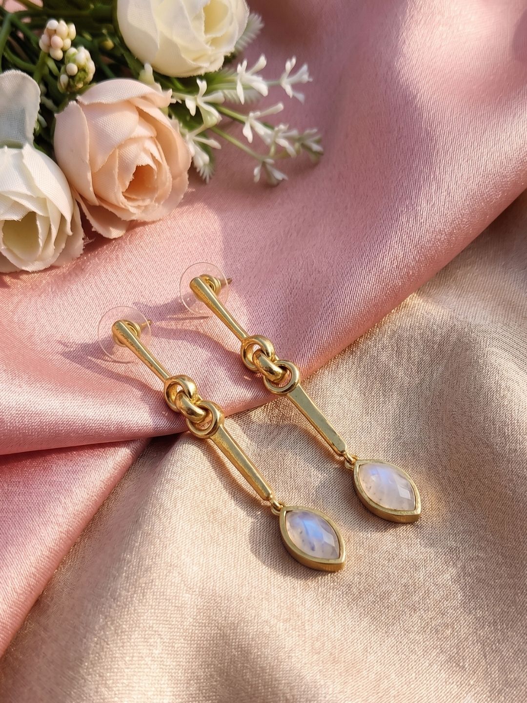 Handcrafted white rainbow gemstone dangle earrings showcased in an artistic decorative arrangement.
