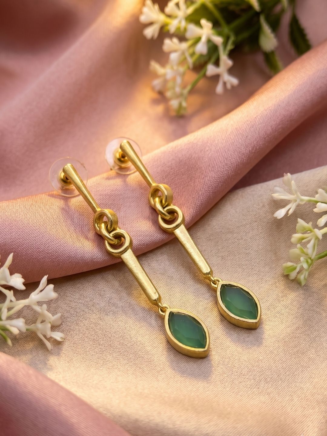 Handcrafted green chalcedony gemstone dangle earrings showcased in an artistic decorative arrangement.
