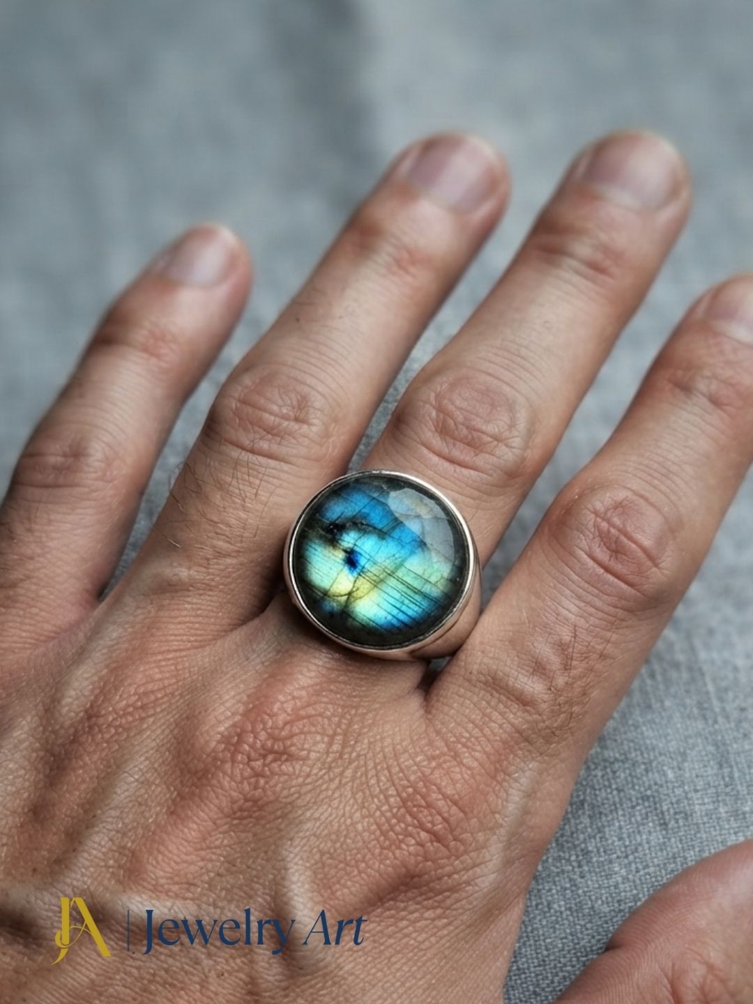 Close-up of a man's hand wearing a natural Labradorite gemstone silver plated GS ring showcasing artisan craftsmanship and elegant design.
