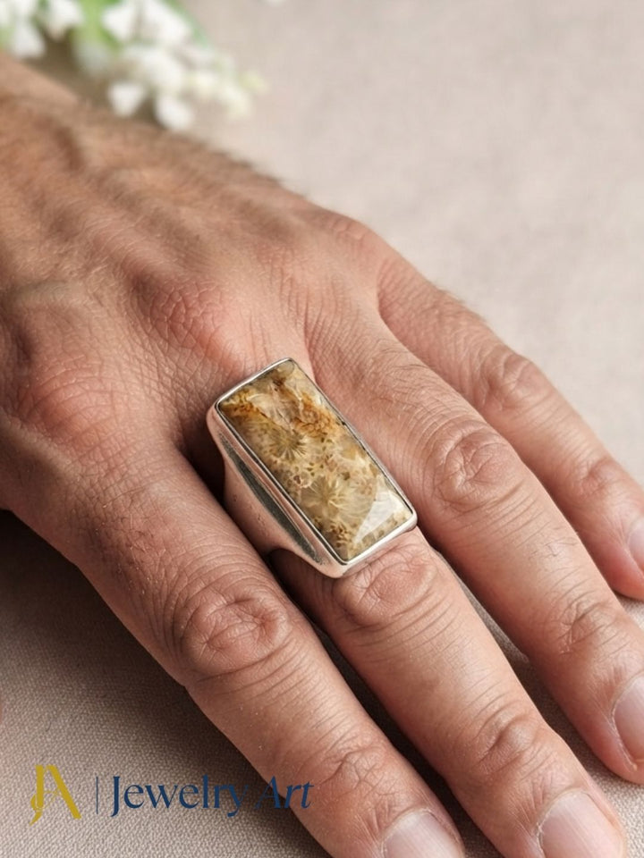 Close-up of a man's hand wearing a Natural Fossil Coral gemstone Silver Overlay GS ring showcasing artisan craftsmanship and elegant design.
