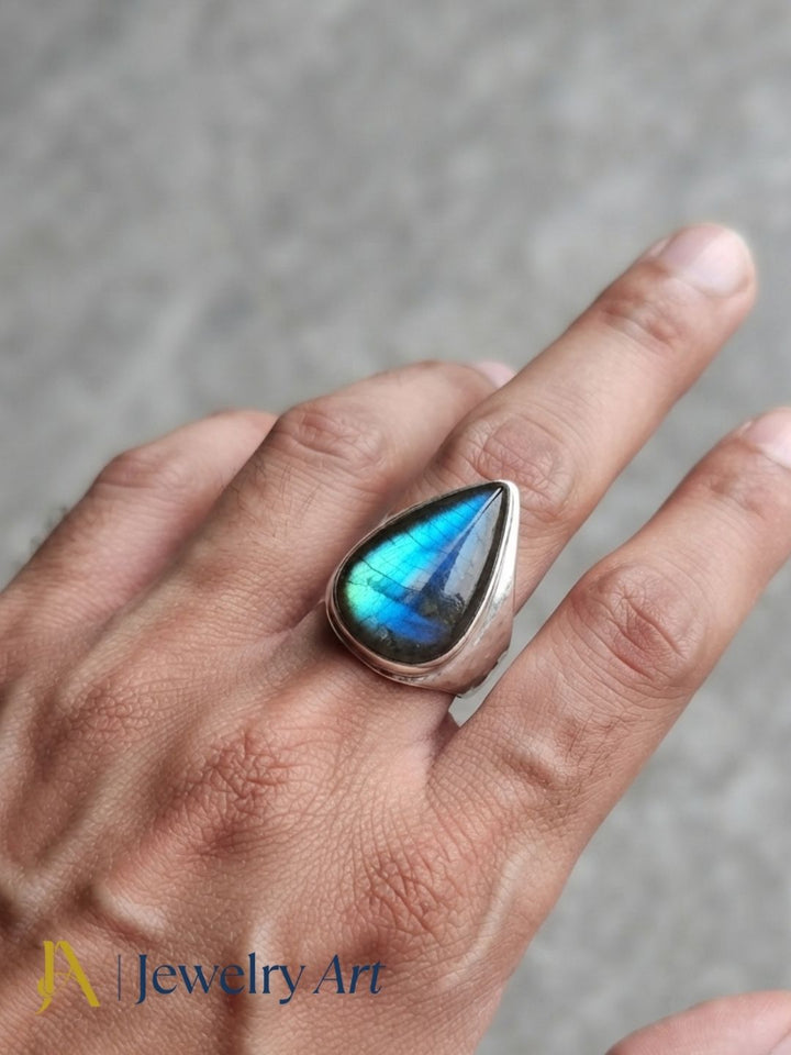 Close-up of a man's hand wearing a natural Labradorite gemstone silver plated GS ring showcasing artisan craftsmanship and elegant design.
